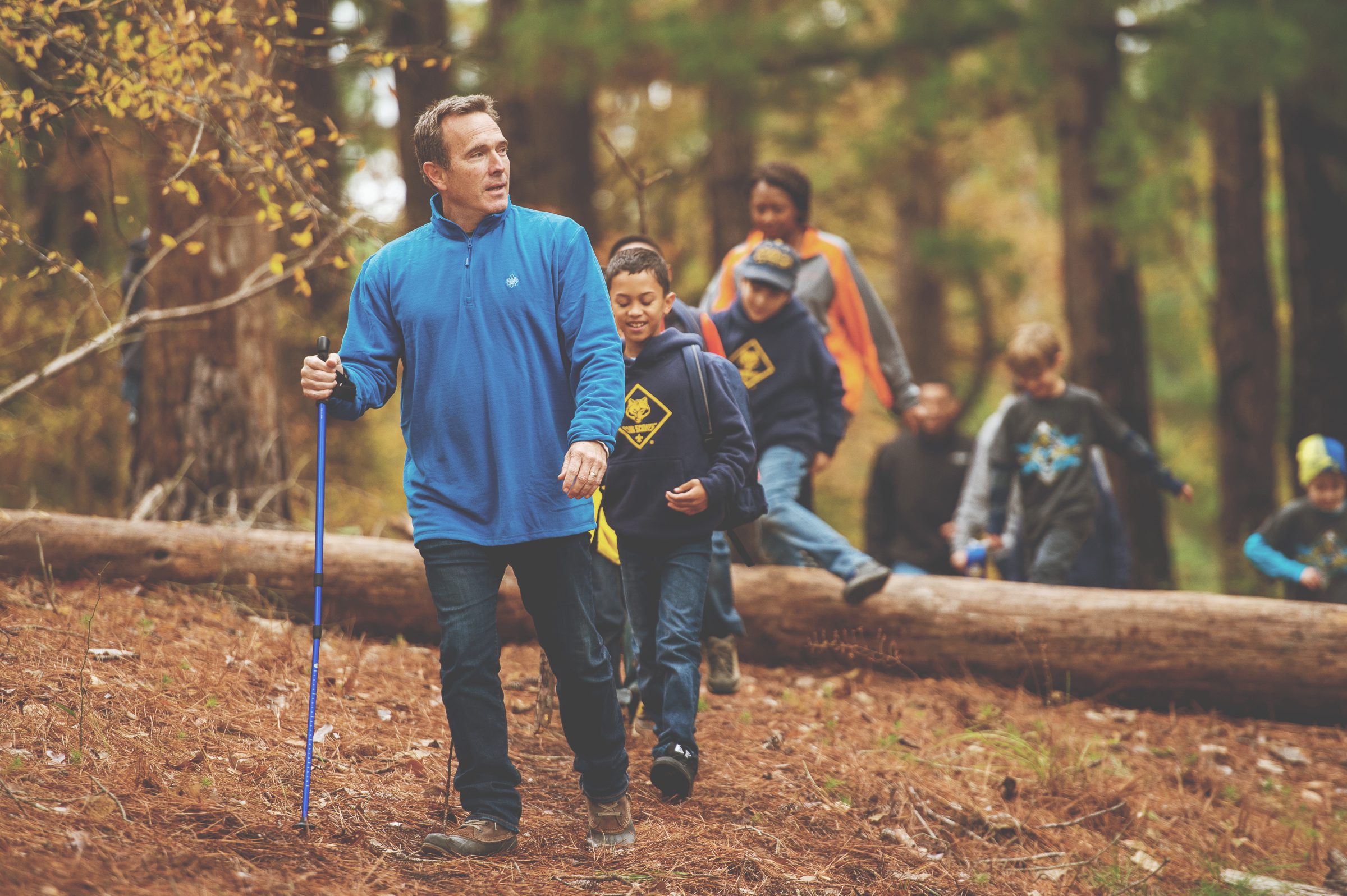 Decorative image of adult male along with cub scouts and another adult leader, hiking in the woods.